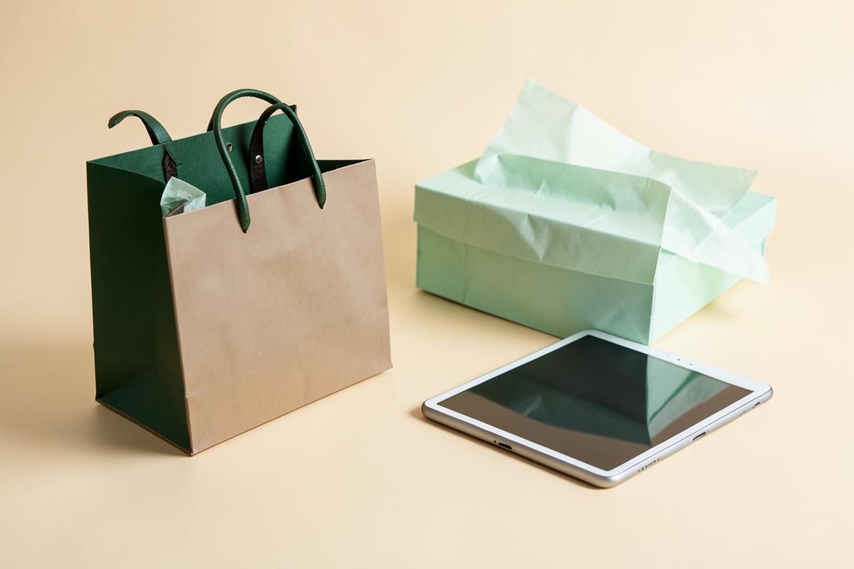 Shopping bag, parcel box and tablet on a cream surface